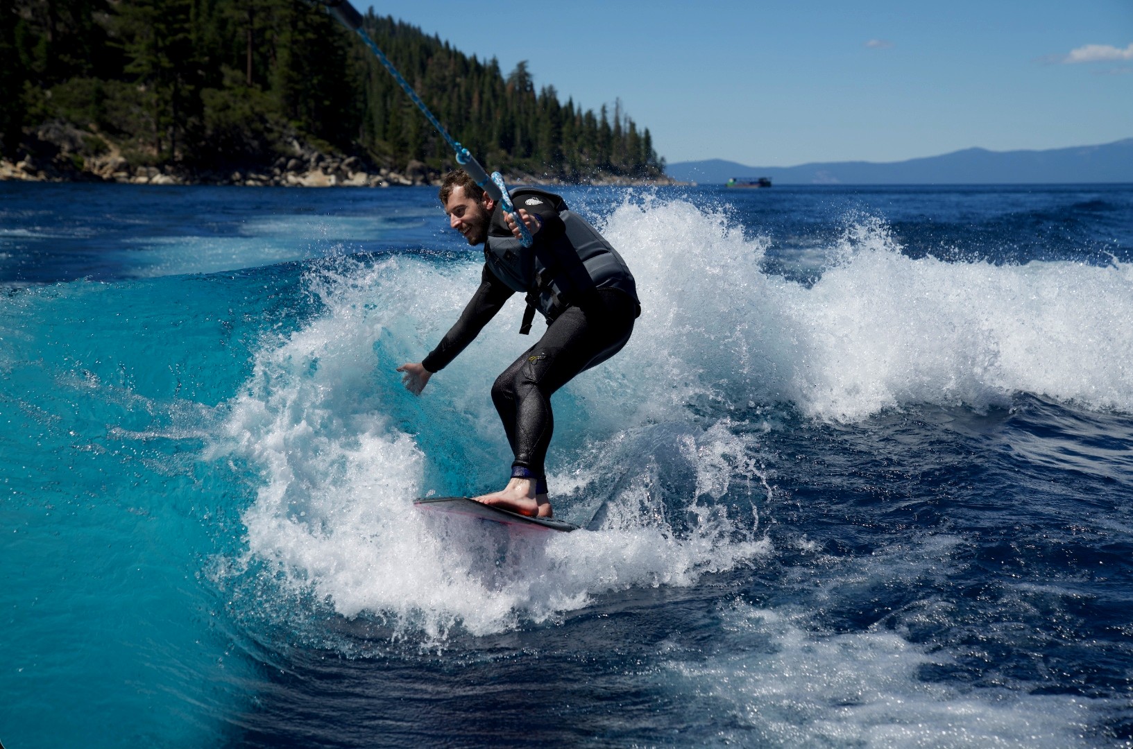 Nicholas wake surfing on a lake surrounded by mountains